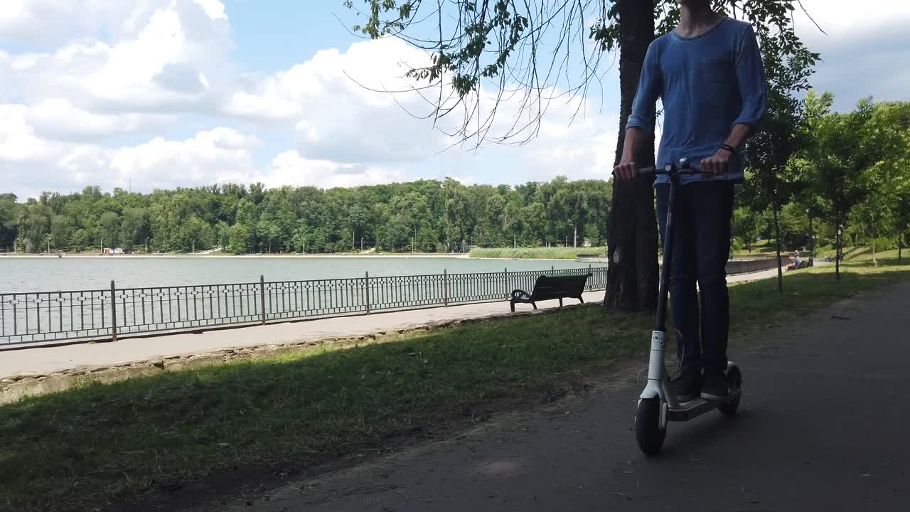 公園で白い電動スクーターに乗る男性。背景には湖。