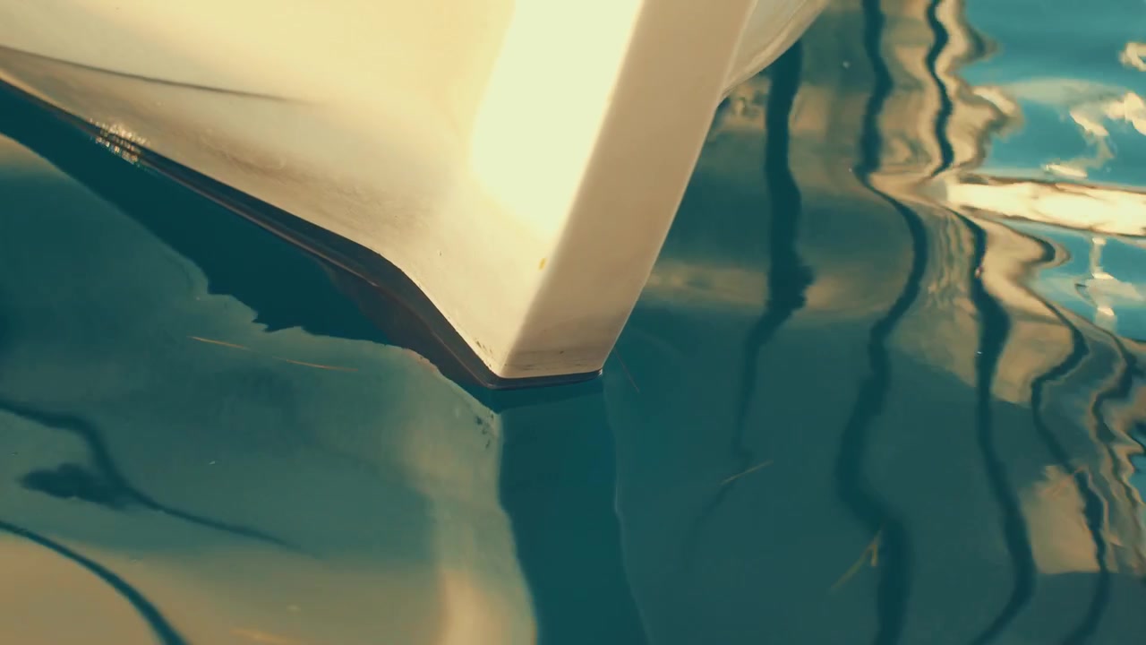 Filmisk vintage abstrakt film av milda havskrusningar som skapar förvrängda, konstnärliga reflektioner av en vit båtstäv på vattenytan