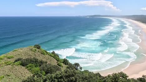 aerial footage showcasing vibrant greenery and rolling ocean waves along a sandy coastline under a clear blue sky.