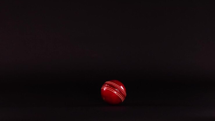 Red cricket ball moving across dark background