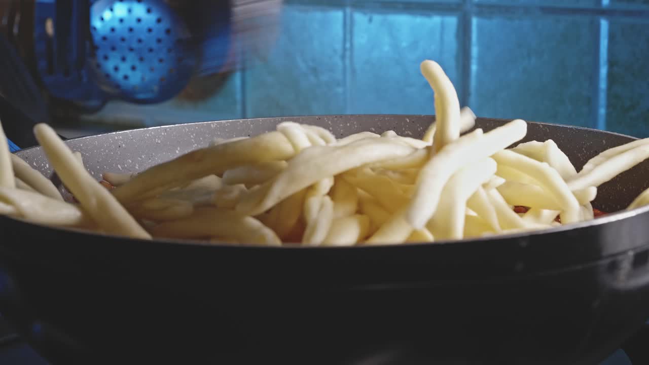 Adding pasta to a pan with vegetarian bolognese sacue on it, close up view
