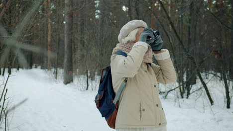 senior woman taking pictures in a snowy forest