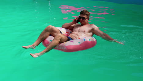 man talking on phone in pool with inflatable ring
