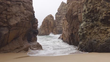 waves coming in through a rocky outcrop in praia da ursa, portugal