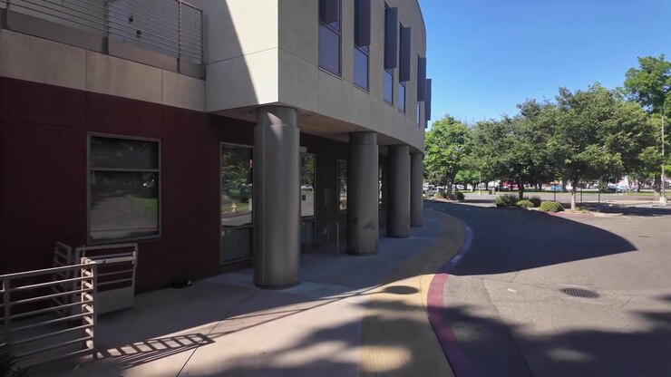 Ripresa in soggettiva mentre si cammina lungo un sentiero nel campus del San Joaquin Delta College a Stockton, California, passando accanto a un moderno edificio curvo in una giornata di sole splendente con cieli azzurri e sereni