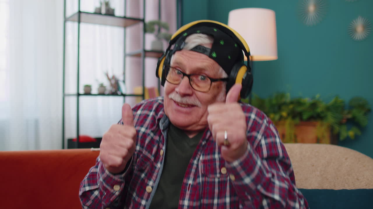 hombre mayor feliz en auriculares inalámbricos bailando, cantando en el sofá acogedor en la sala de estar en casa