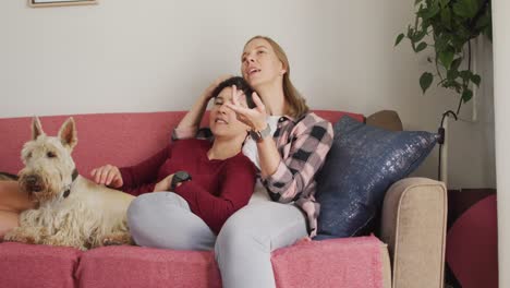pareja de lesbianas caucásicas hablando entre sí sentados en el sofá con su perro en casa
