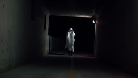 una persona que se pone una sábana blanca sobre la cabeza y se pone gafas de sol para parecer un disfraz de fantasma genial para halloween en un pequeño túnel por la noche en provo, utah, en una fría noche de otoño