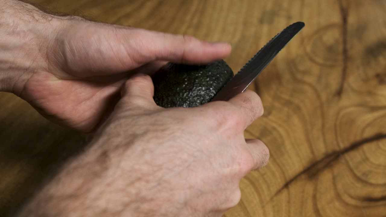 나무 테이블 배경 에 아보카도 를 잘라내는 젊은 남자