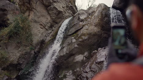 cámara lenta de un excursionista usando su teléfono para tomar fotos de una cascada que fluye entre formaciones rocosas