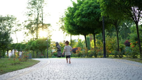 barefoot baby boy sitting on the paved alley stands up. toddler runs by the road distancing from camera.