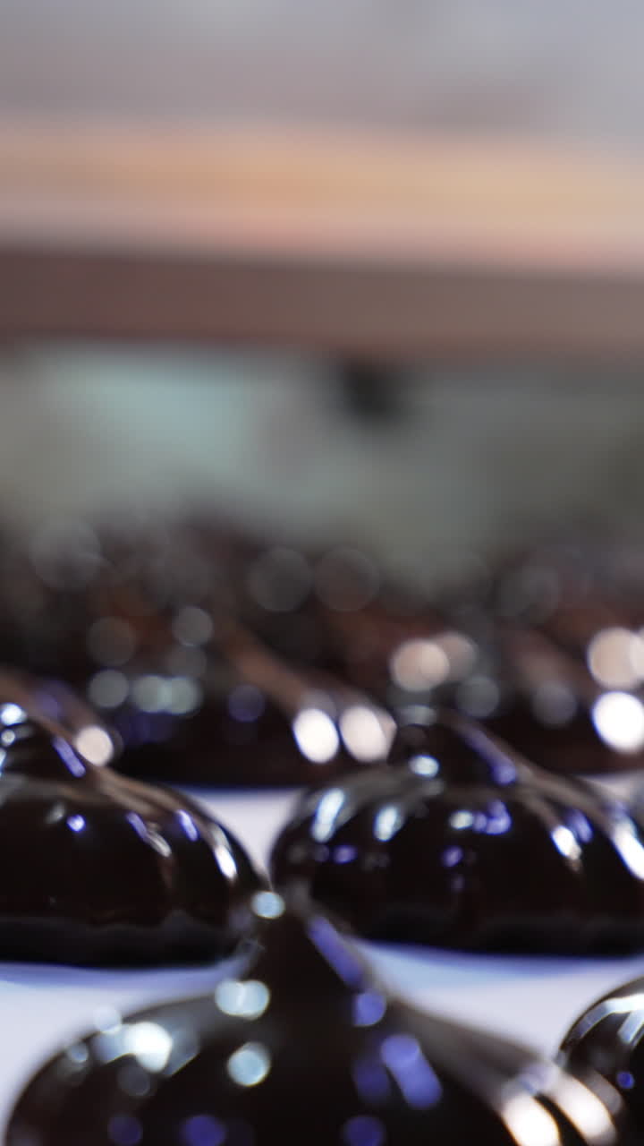 Zephyr candies coated in black chocolate. Ready-made chocolate desserts move on the conveyor belt. Close up. Vertical video