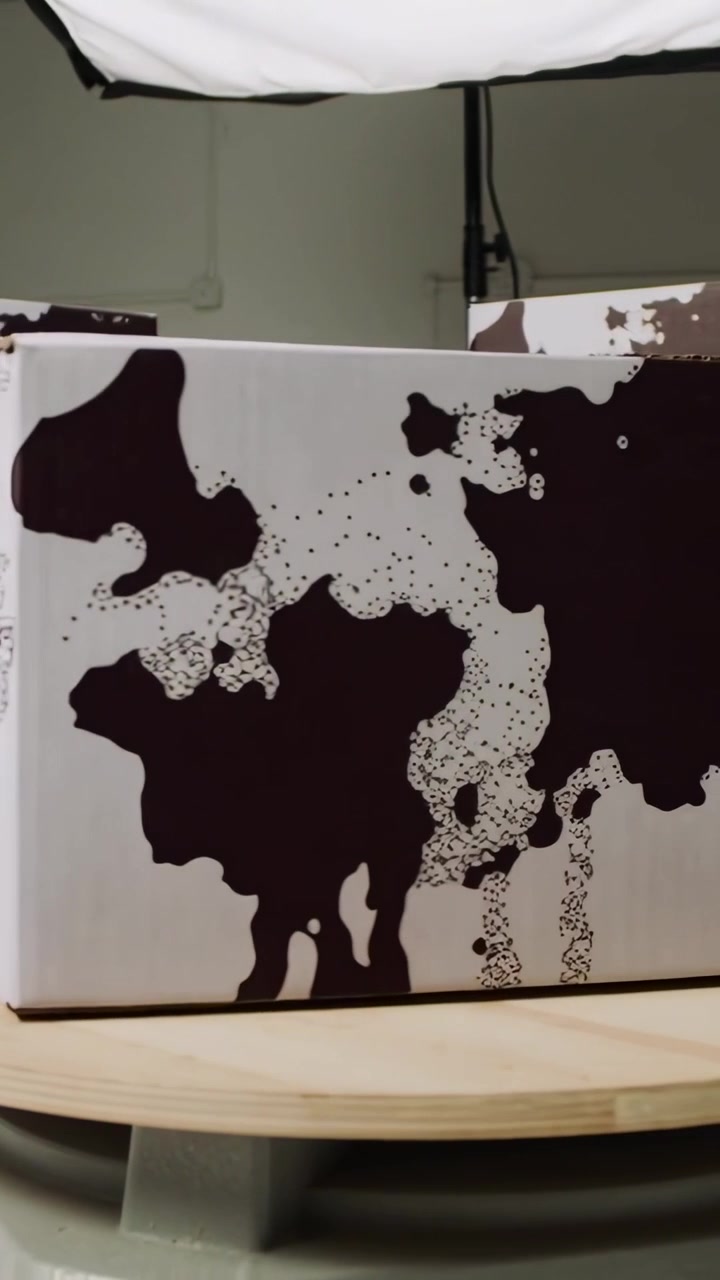 Video verticale: Piattaforma girevole che inizia a ruotare, spostando una scatola a fantasia su un tavolo da studio per scatti di prodotti.