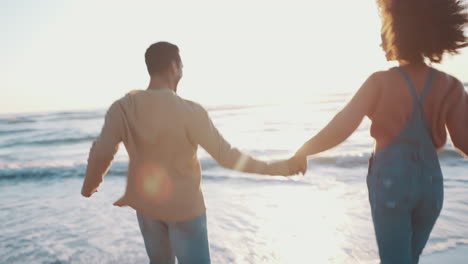 pareja, tomados de la mano y corriendo hacia el océano