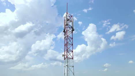 red and white 5g cell phone tower with blue sky and white clouds in the background