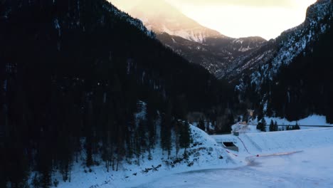 Up-tilting-aerial-drone-shot-of-a-winter-landscape-of-Mount-Timpanogos-in-the-background-surrounded-by-a-pine-tree-forest-during-sunset-from-Tibble-Fork-Reservoir-in-American-Fork-Canyon,-Utah