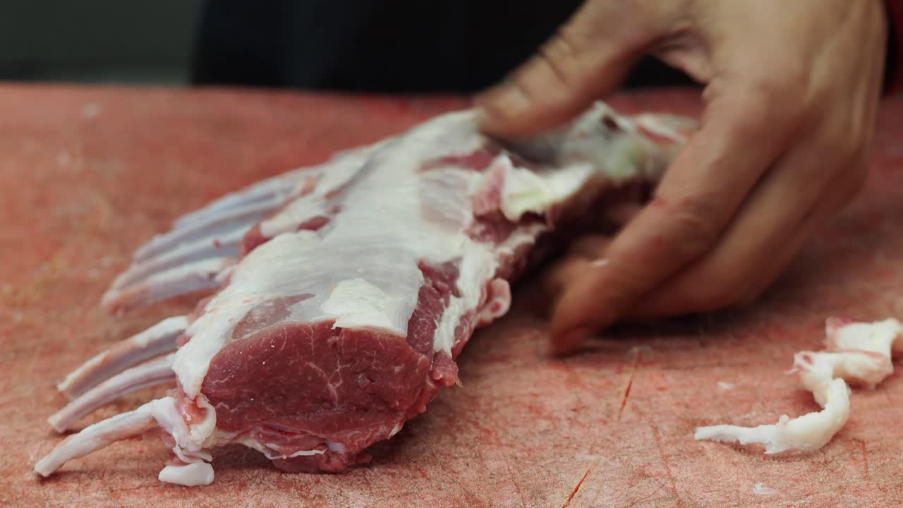 Macellaio che rifila il grasso da un carré di agnello crudo con un coltello