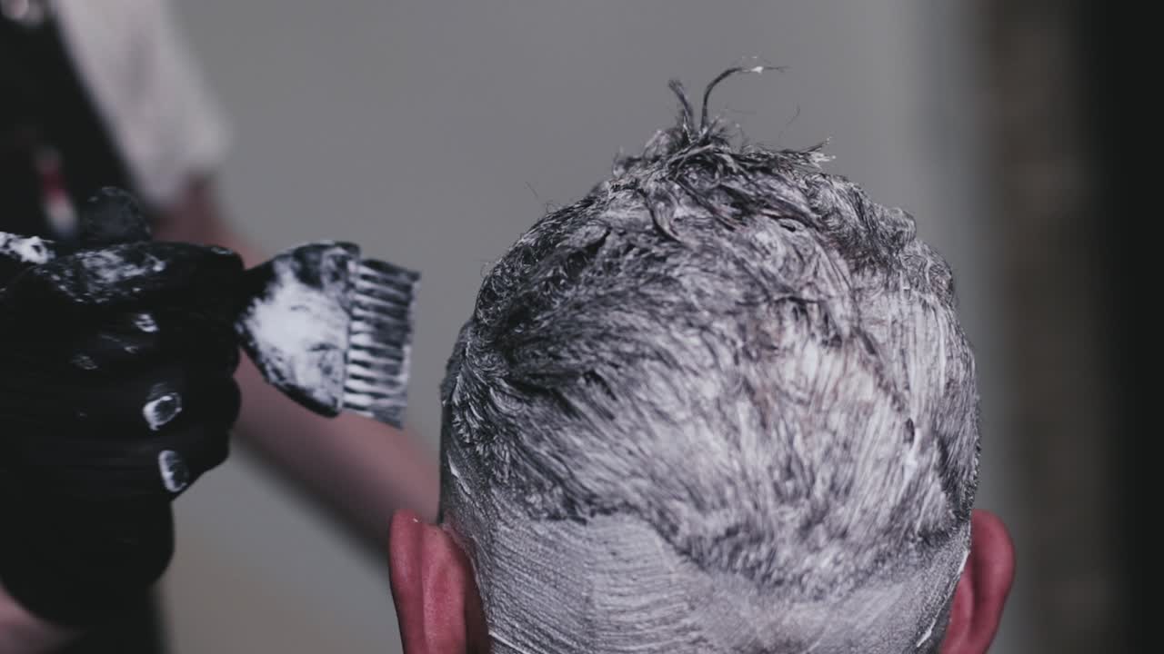 Parrucchiere che tinge i capelli di un cliente con un pennello