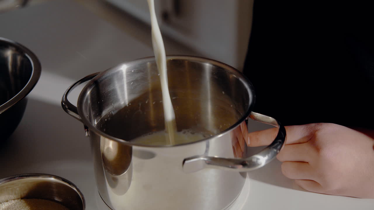 Giovane donna che versa il latte in una pentola mentre prepara l'impasto per una torta in cucina a casa.