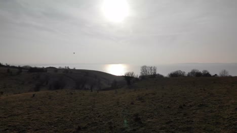 Aerial-view-of-beautiful-green-hills,-moving-toward-the-sunset-above-the-blue-sea-in-Sejerøbugten,-Denmark