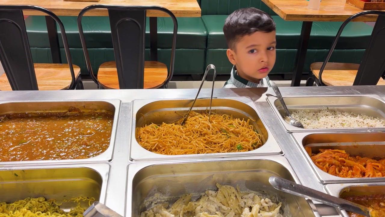Bambino in piedi vicino al bancone del buffet di un ristorante, che presenta le opzioni alimentari e il concetto di ristorazione.