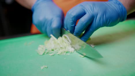 hands with plastic gloves chop lettuce with knife in kitchen, close-up