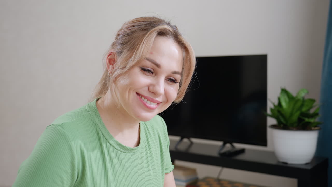 Mother touches son gently on nose while he sleeps under blanket as she smiles warmly expressing love care and affection in cozy bedroom with television and plant in background