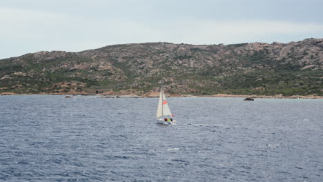 Segelboot-Gleitet-Auf-Dem-Azurblauen-Meer-Sardiniens-Mit-Bergen-Im-Hintergrund