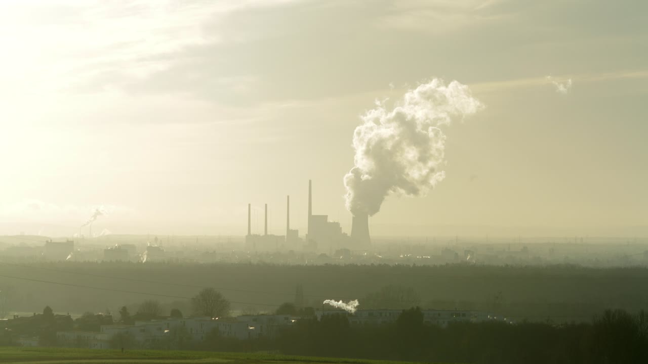 Time-lapse of a powerplant as it pushes out steam with clouds moving behind it in a hazy smoggy atmosphere