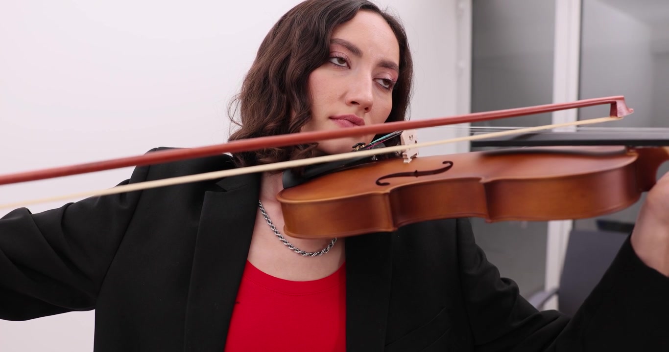 Young woman in black jacket intently plays violin holding bow