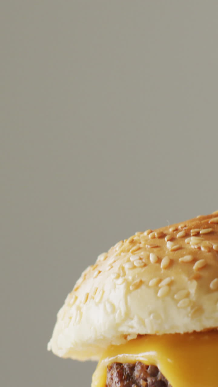 video de primer plano de una hamburguesa con queso con ensalada en un pan de hamburguesa, en un fondo gris pálido con espacio para copiar