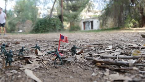 a boy playing alone outdoors throws a rock past his display of green army man toys