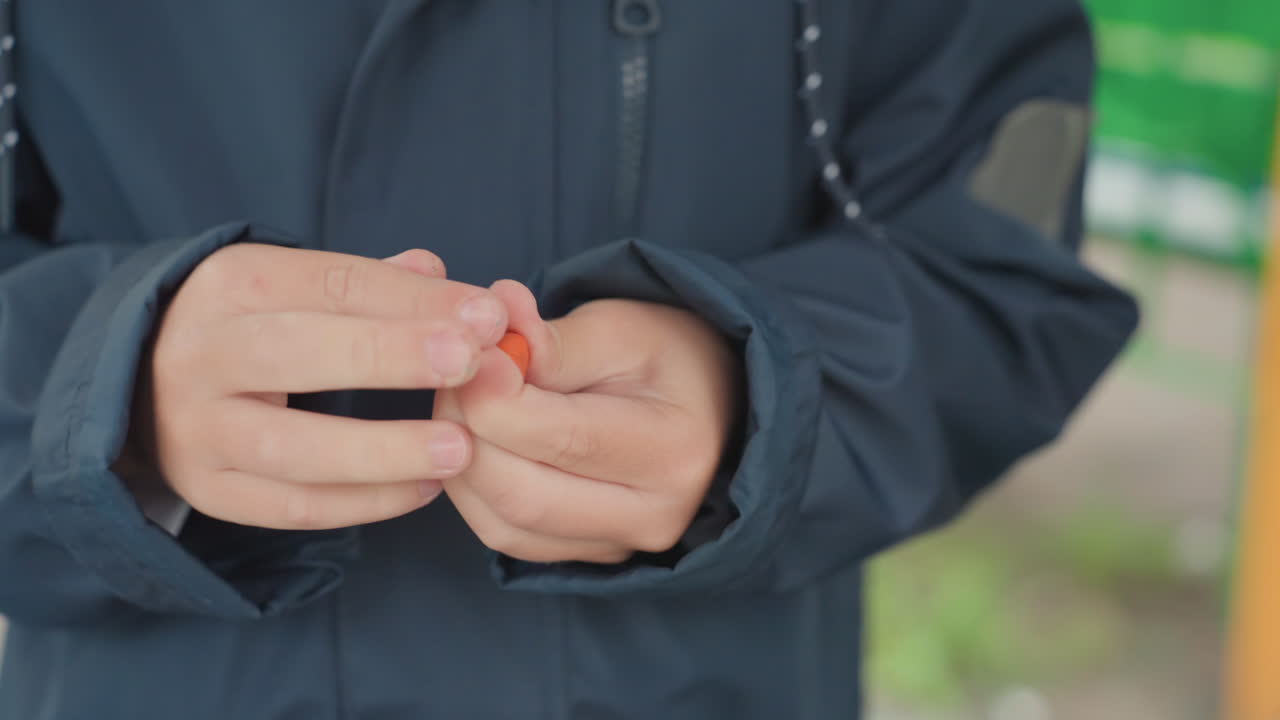 Close-up tangan menyiapkan jaket kembali ke sekolah, siswa gelisah dengan kancing dan ritsleting sambil menunggu di luar ruangan, lengan jaket biru tua, kedalaman bidang dangkal, energi gugup halus dan suasana rutinitas pagi.