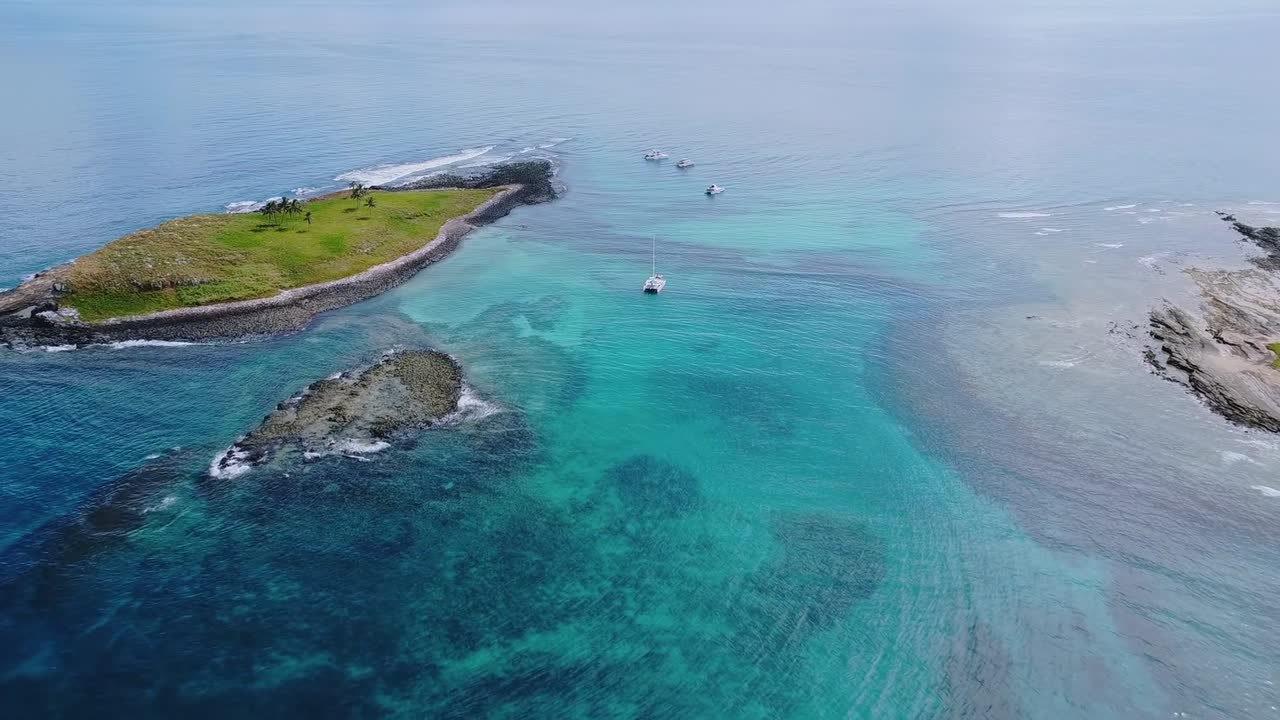 Arcipelago di Abrolhos che mostra una prospettiva aerea di vivaci acque turchesi che abbracciano isole verdi lussureggianti, formando coste rocciose naturali nell'Oceano Atlantico meridionale.