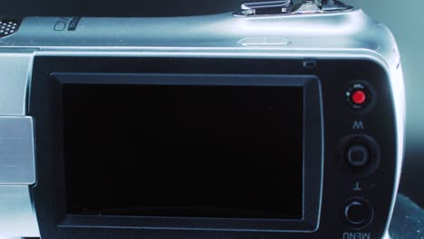 un primer plano de una cámara de video, una videocámara plateada en un soporte giratorio de 360 grados, iluminación de estudio, video de 4k en cámara lenta, pantalla volteada, botones de grabación y menú