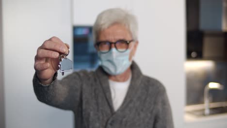 portrait of senior man wearing face mask show keys to new home