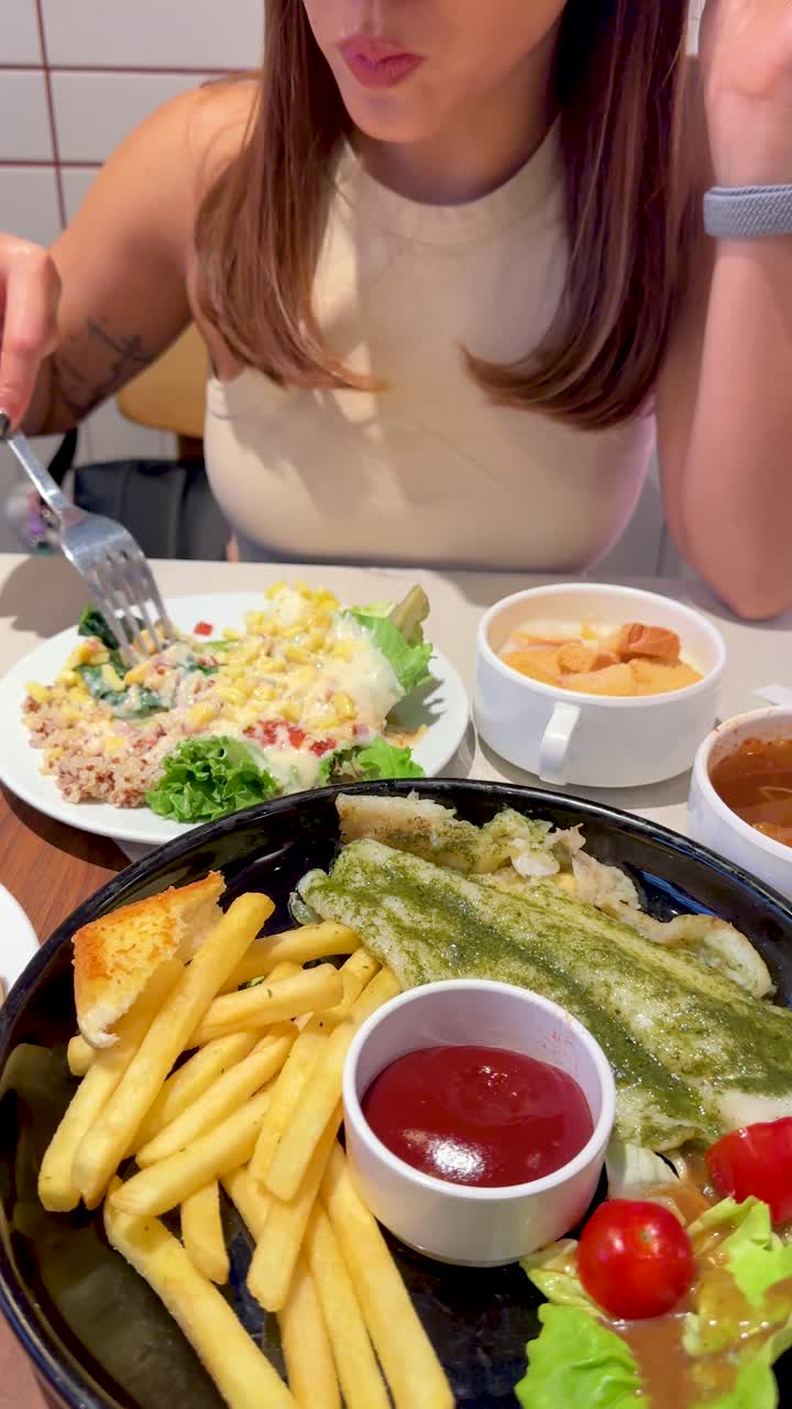 明るいバンコクのレストランで、若い女性がフライドポテトとサラダ添えのフィッシュステーキを食べるクローズアップ。