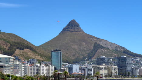 Paragliding-hang-glide-flying-off-Table-Mountain-Lions-Head-downtown-city-skyscraper-buildings-to-Cape-Town-beach-South-Africa-summer-adventure-beautiful-calm-wind-still-morning-slow-motion-follow