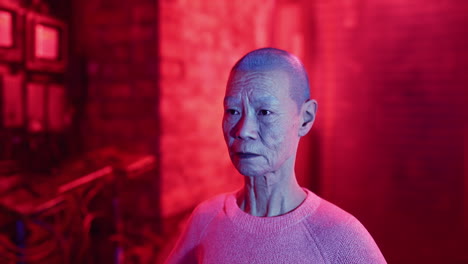 portrait of an elderly asian woman with shaved head in red lighting