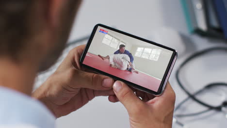 composición de un médico masculino viendo un partido de judo en un teléfono inteligente