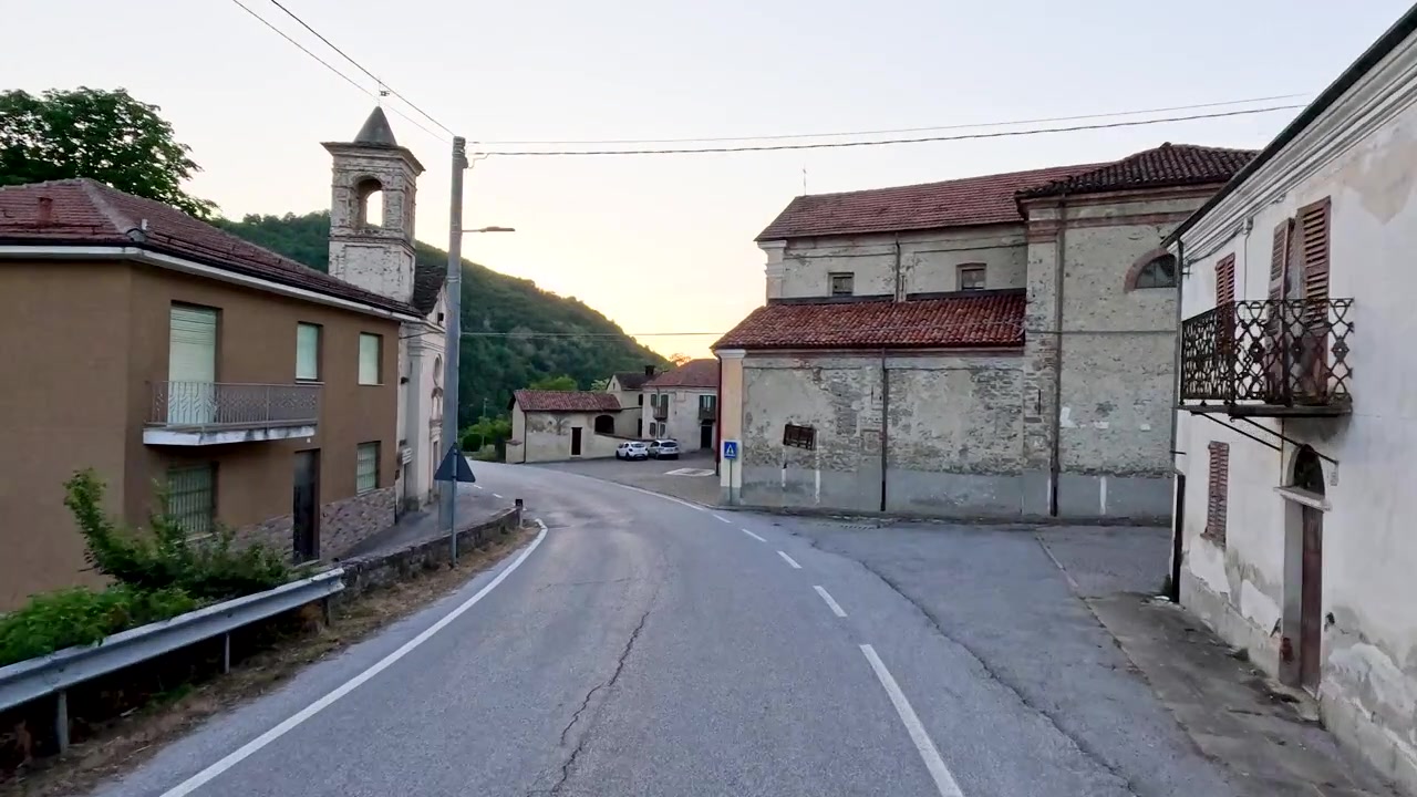 A smooth camera movement follows an asphalt road into a historic stone village at dusk.