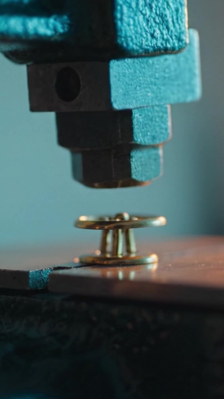 Close-Up of Metal Press Mechanism Embedding a Gold Button into Fabric, Showcasing Details of the Process and Textures in a Workshop Environment