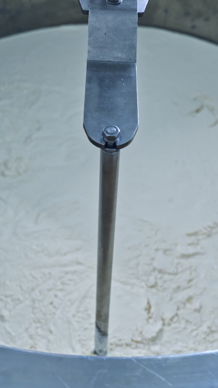 Factory equipment close-up. Metal mixing apparatus boils and mix milk for making cheese at milk products making factory in slow motion. Vertical video