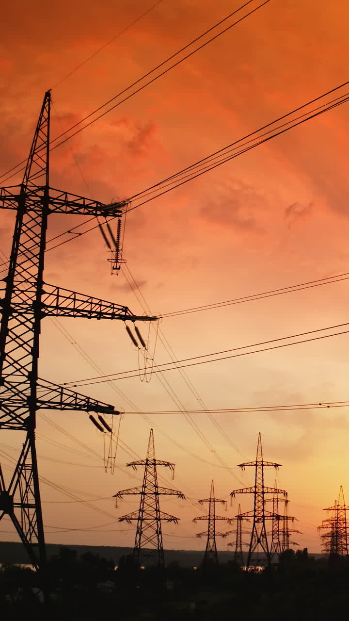 Electricity distribution station at sunset. High steel electric towers with wires on bright evening sky backdrop. Hi-voltage power lines. Rising up. Vertical video