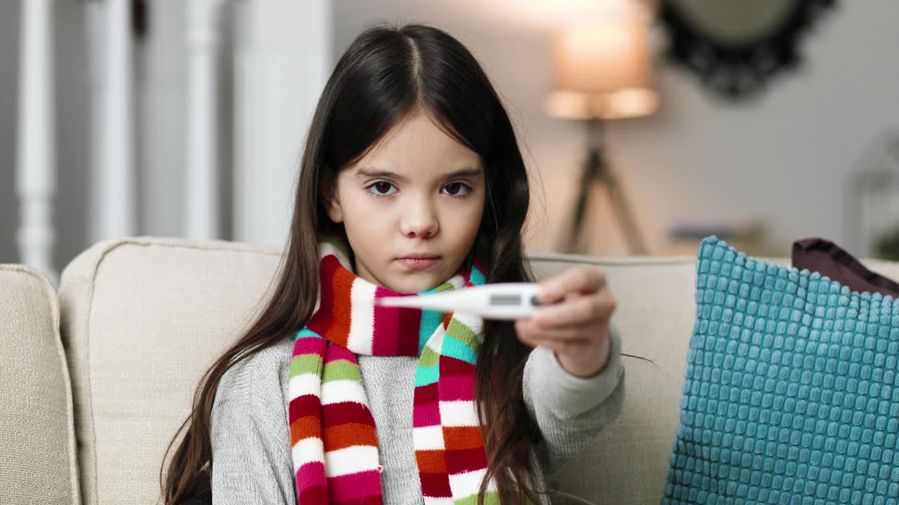 Close up portrait of sick little child using a thermometer while sitting in a room