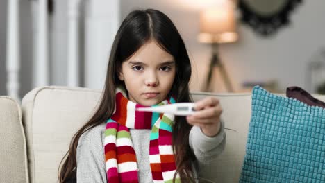 Close-up-portrait-of-sick-little-child-using-a-thermometer-while-sitting-in-a-room