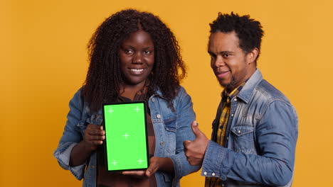 african american couple pointing at a tablet with isolated green screen display