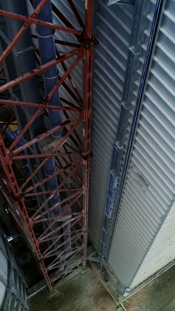 Metal brown tower with tube inside attached to a silo tank and warehouse. Descending footage along the granary premises. Top view. Vertical video
