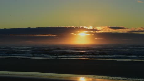 Dramatic-view-across-a-deserted-beach-with-a-stunning-golden-sunrise-or-sunset-with-a-silhouetted-4x4-truck-driving-past-with-fishing-gear