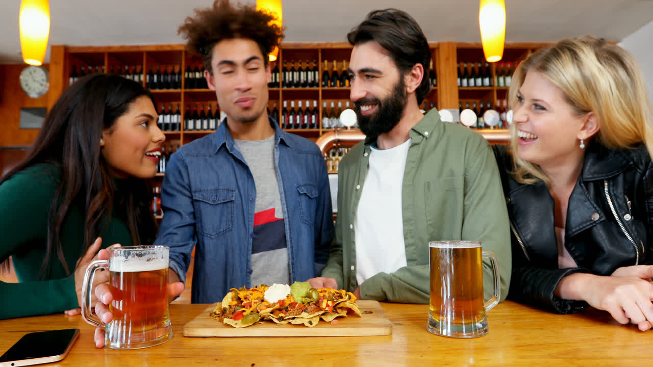 amigos tomando un vaso de cerveza y comida mexicana en el bar 4k